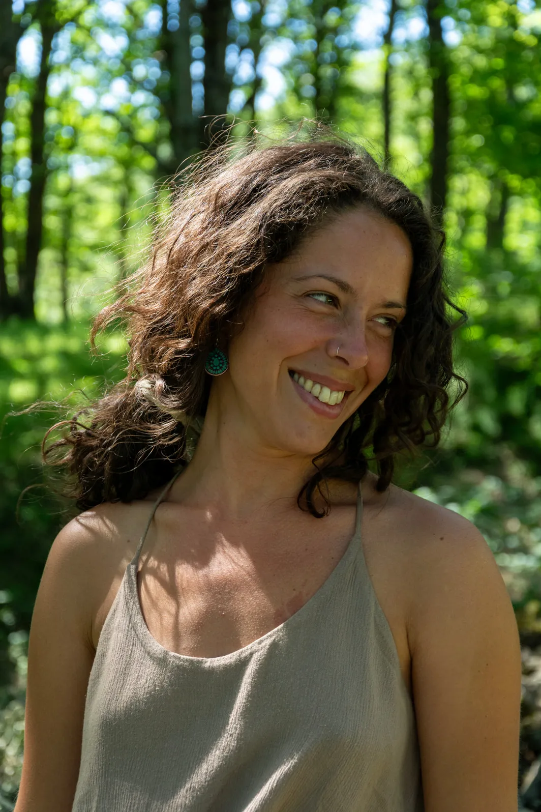 Portrait of Roberta Martini outdoors, smiling and looking to one side, with sunlit woodland behind her
