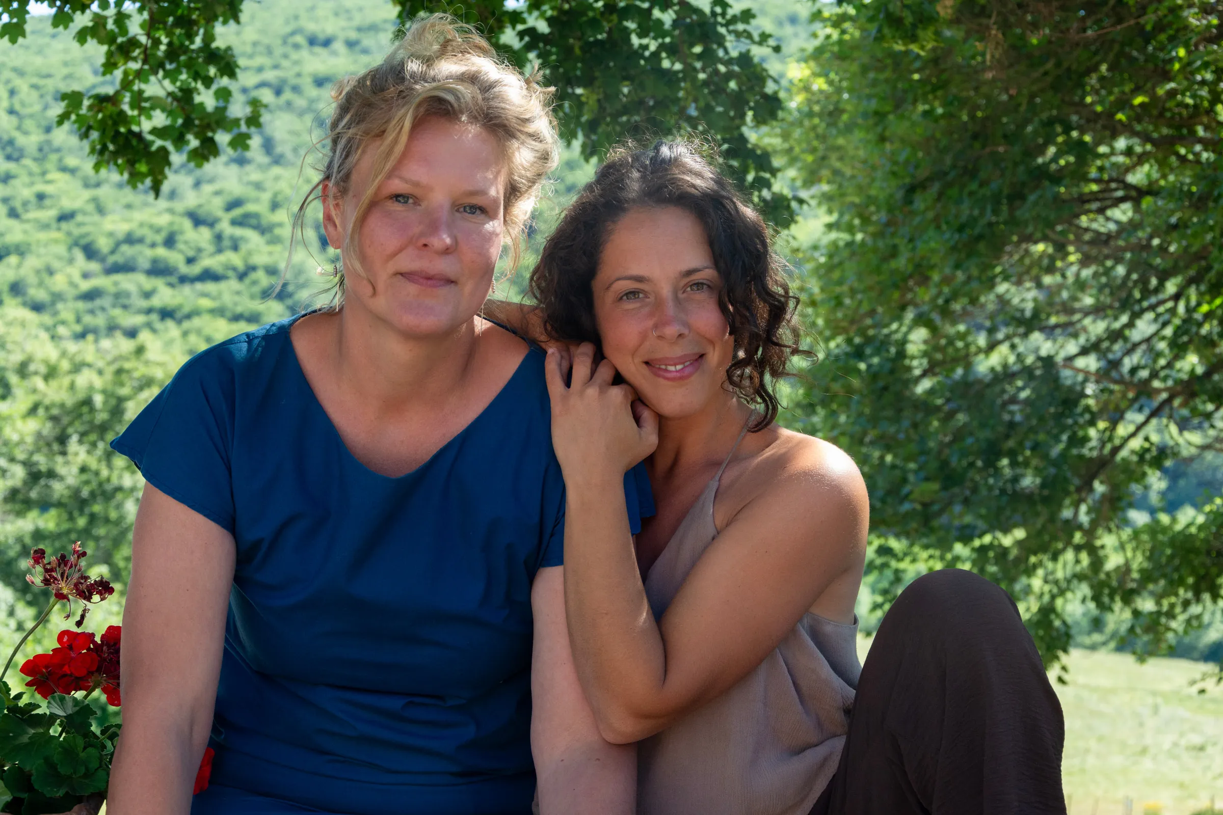 Isabelle and Roberta sitting close together outdoors, wooded hills behind them