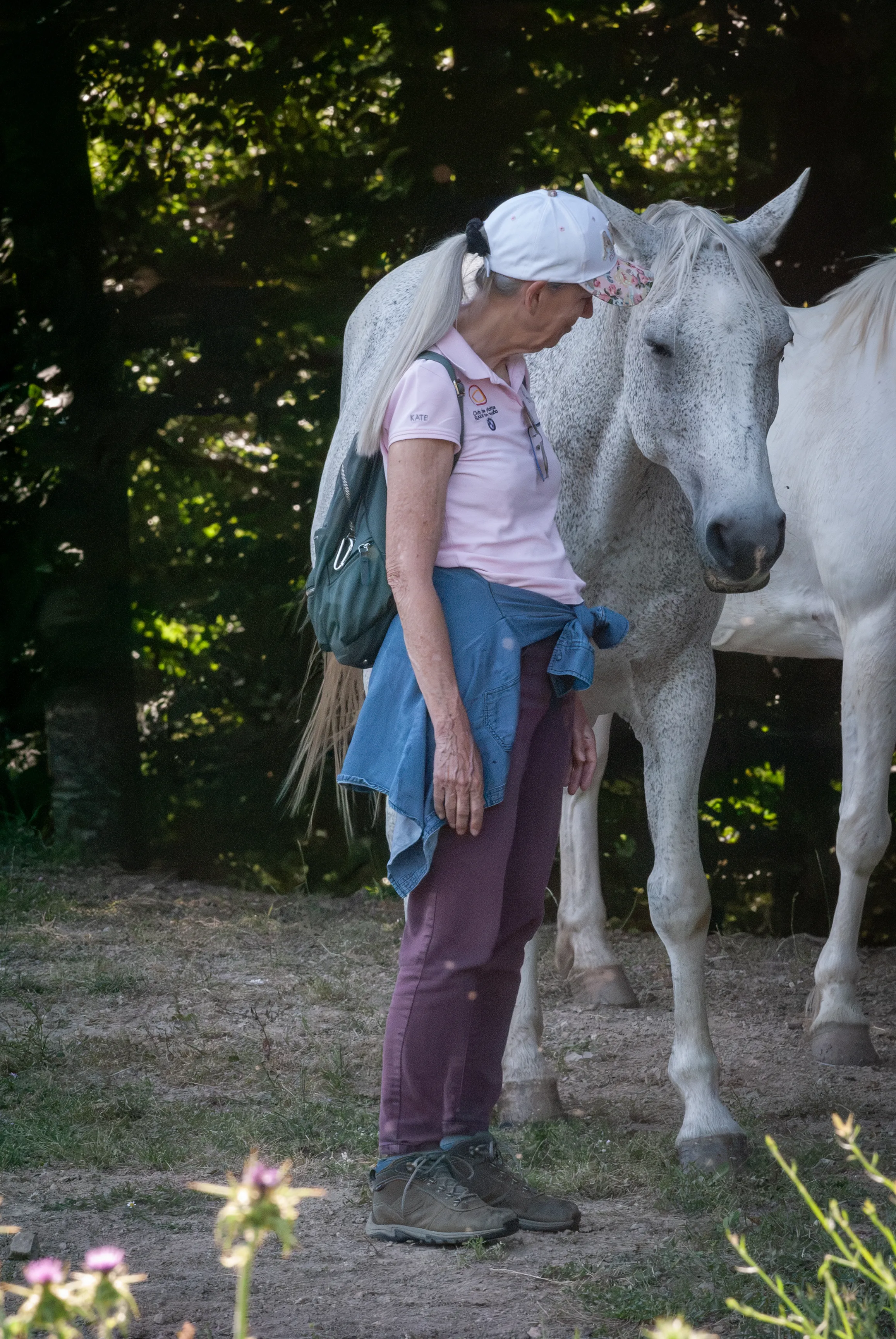 A woman standing quietly beside a white horse at the forest edge