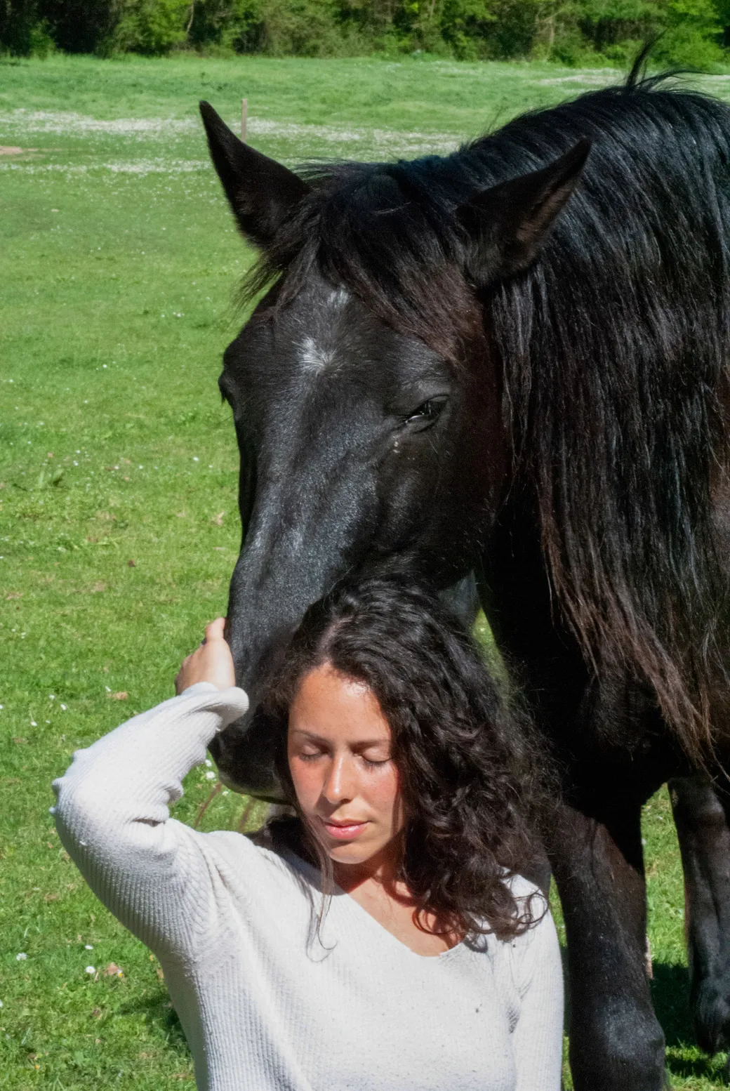 A woman with her eyes closed resting her hand on the face of a black horse leaning towards her